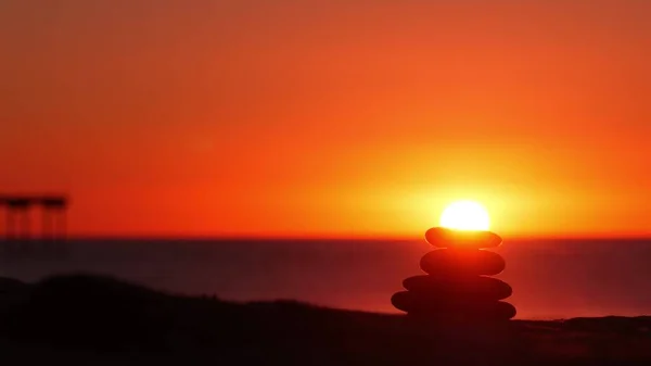 Stack of pebble stones, sandy ocean beach, sunset sky. Rock balancing by water. — Stock Photo, Image