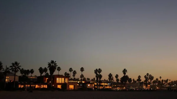 Kaliforniya sahillerinde, alacakaranlık gökyüzünde palmiye ağaçları siluetleri. Sahildeki evler — Stok fotoğraf