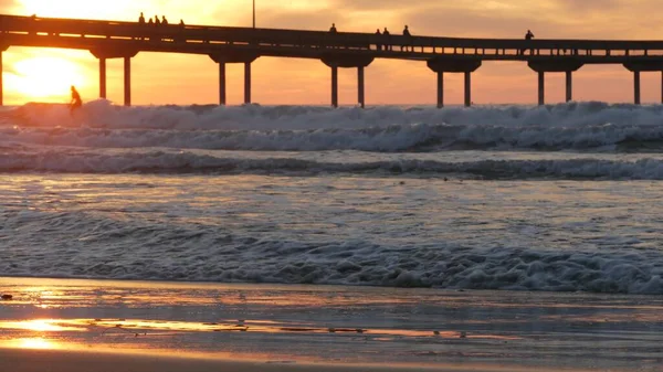 Surfistas a surfar por cais. Ondas de água do oceano, pessoas e céu ao pôr-do-sol. Califórnia — Fotografia de Stock