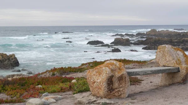 Felsige zerklüftete Meeresküste, Meereswellen, Monterey Kalifornien. Holzbank leer. — Stockfoto