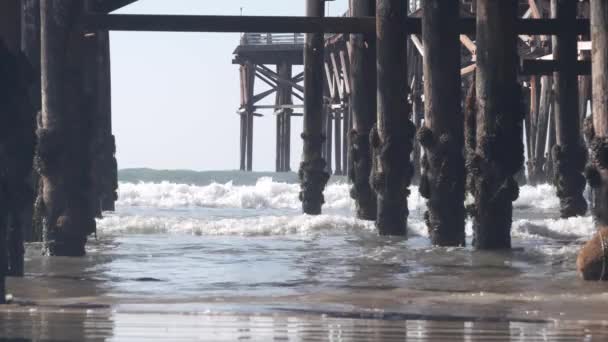 美国加利福尼亚，在木制水晶码头下面的沙堆上，海滩上的水波. — 图库视频影像