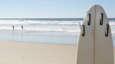 Kaliforniya sahillerinde sörf yapmak için sörf tahtası. Okyanus dalgası ve beyaz sörf tahtası veya kürek tahtası. Deniz suyuyla su sporu yapmak için uzun tahta ya da yemek. Yaz tatili, sahilde spor.