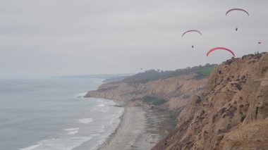 İnsanlar yamaç paraşütü yapıyor, Torrey Pines uçurumu ya da blöf. Paraglider paraşüt, uçurtma ya da kanatla gökyüzünde süzülüyor. Spor hobisi. Okyanus kıyısı, San Diego, Kaliforniya ABD. Paraşütle uçmak riskli. Kuşlar uçuyor.