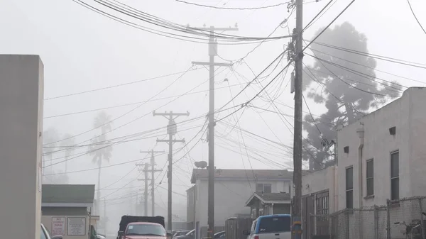 電線または電柱 霧の多い街 カリフォルニア州 米国のワイヤ 霧のサンディエゴで高電圧木製の電気ポストやパイロン上のケーブル アメリカの電力供給と住宅 — ストック写真