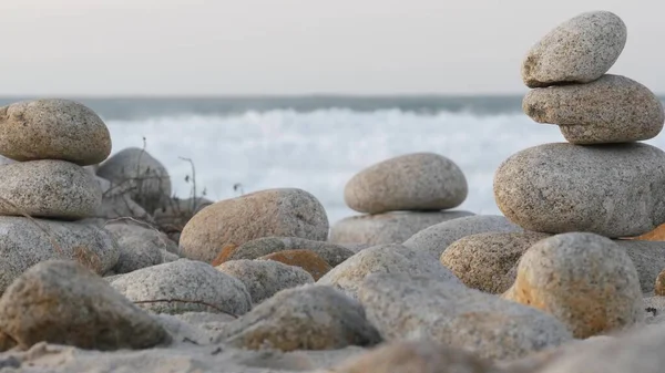 Rock balance on pebble beach, Monterey 17-mile drive, California coast, USA. Stable pyramid stacks of round stones, sea ocean water waves crashing at sunset. Zen meditation Seamless looped cinemagraph