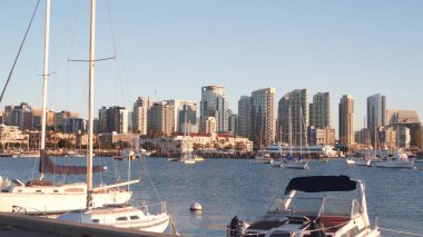 Yat marinada ve şehir merkezinde günbatımında ufuk çizgisi, San Diego şehir manzarası, California sahili, ABD. Yükselen gökdelenler, körfezde bir tekne, rıhtım güvertesi. Limanda kentsel mimari ve yelkenli.