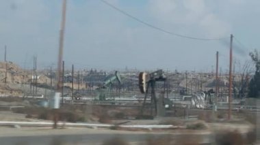 Kaliforniya, ABD 'de petrol sahasında pompalı valeleri olan kuyular. Petrol sahasında çalışan ham fosil çıkarma ekipmanları. Endüstriyel arazi, çöl vadisindeki raylar. Petrol kuyularında pompalayan birçok pompa platformu.