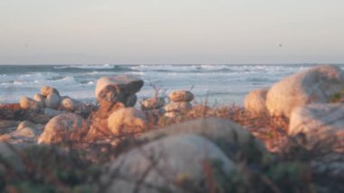Çakıl taşı plajında kaya dengesi, Monterey 17 mil sürüş, Kaliforniya kıyısı, ABD. Yuvarlak taşların durağan piramit yığınları, gün batımında deniz suyu dalgaları çarpıyor. Huzur uyumu, sakinlik meditasyonu.