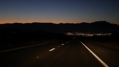 Gece çöl yolunda giden araba, alacakaranlıkta giden otoyol, ön camdan ya da ön camdan bakan bakış açısı. Kaliforniya 'ya yolculuk. Ufukta vadi ve dağlar var..
