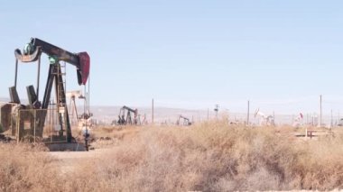 Kaliforniya, ABD 'de petrol sahasında pompalı valeleri olan kuyular. Petrol sahasında çalışan ham fosil çıkarma ekipmanları. Endüstriyel arazi, çöl vadisindeki raylar. Petrol kuyularında pompalayan birçok pompa platformu.