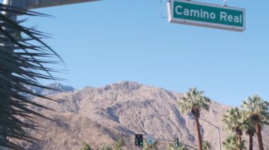 Palmiye ağaçları ve gökyüzü, Palm Springs sokağı, Los Angeles yakınlarındaki şehir, kavşaktaki semafor trafik ışıkları. California çöl vadileri, yaz yolculukları arabayla, Amerika seyahatleri. Dağ. Camino Gerçek Yol İşareti