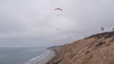 İnsanlar yamaç paraşütü yapıyor, Torrey Pines uçurumu ya da blöf. Paraglider gökyüzünde süzülüyor, paraşütle, uçurtmayla veya kanatla uçuyor. Eğlence amaçlı spor hobisi. Okyanus kıyısı, San Diego, Kaliforniya ABD. Paraşüt uçuşu