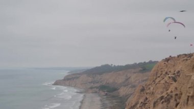 İnsanlar yamaç paraşütü yapıyor, Torrey Pines uçurumu ya da blöf. Paraglider paraşüt, uçurtma ya da kanatla gökyüzünde süzülüyor. Spor hobisi. Okyanus kıyısı, San Diego, Kaliforniya ABD. Paraşütle uçmak riskli. Kuşlar uçuyor.