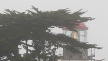 Pinos eski tarihi deniz feneri mercekleri parlıyor, sisli yağmurlu kötü hava. Aydınlatılmış antika ışık evi ya da fener kulesi, sisli selvi çam ağacı ormanı. Monterey, Kaliforniya kıyısı ABD