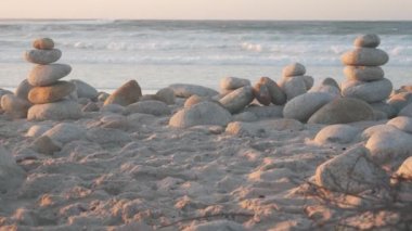 Çakıl taşı plajında kaya dengesi, Monterey 17 mil sürüş, Kaliforniya kıyısı, ABD. Yuvarlak taşların durağan piramit yığınları, gün batımında deniz suyu dalgaları çarpıyor. Huzur uyumu, sakinlik meditasyonu.