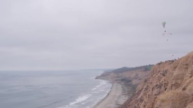 İnsanlar yamaç paraşütü yapıyor, Torrey Pines uçurumu ya da blöf. Paraglider gökyüzünde süzülüyor, paraşütle, uçurtmayla veya kanatla uçuyor. Eğlence amaçlı spor hobisi. Okyanus kıyısı, San Diego, Kaliforniya ABD. Paraşüt uçuşu