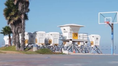 Palmiye ağaçları ve basketbol sahası veya Kaliforniya sahillerindeki saha, ABD. Sahilde sokak topu sahası ve cankurtaran durağı, ot istasyonu. Mission Sahili, San Diego. Hoop, sedye ve gökyüzü.