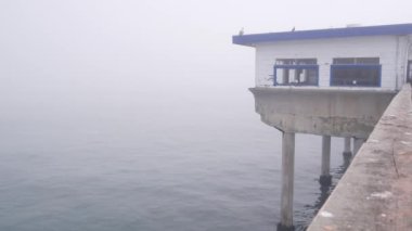 Yığınlar üzerinde ahşap ev, sisli su yüzeyi, Ocean Beach rıhtımı, sisli California sahili, ABD. Sisli havada terk edilmiş eski bir sahil yolu kafesi. San Diego sahilinde sakin, sessiz bir atmosfer..
