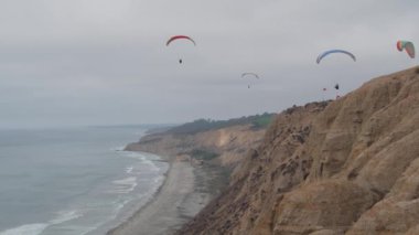 İnsanlar yamaç paraşütü yapıyor, Torrey Pines uçurumu ya da blöf. Paraglider gökyüzünde süzülüyor, paraşütle, uçurtmayla veya kanatla uçuyor. Eğlence amaçlı spor hobisi. Okyanus kıyısı, San Diego, Kaliforniya ABD. Paraşüt uçuşu