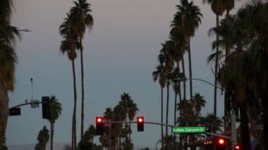 Palm Springs Caddesi 'ndeki palmiye ağaçları, Los Angeles yakınlarındaki şehir, kavşaktaki semafor trafik ışığı. California yaz gezisi arabayla, Amerika seyahati. Yol tabelası, Hint Kanyonu, alacakaranlık gökyüzü, gün batımından sonra alacakaranlık