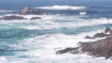 Kayalık okyanus plajı. Büyük dalgalar kayalıklara çarpıyor, mavi su sıçrıyor, deniz köpüğü. Big Sur yakınlarında doğanın gücü, 17 millik yol. Dramatik deniz manzarası. Point Lobos, Monterey, California sahili, ABD