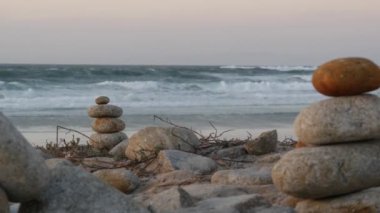 Çakıl taşı plajında kaya dengesi, Monterey 17 mil sürüş, Kaliforniya kıyısı, ABD. Yuvarlak taşların durağan piramit yığınları, gün batımında deniz suyu dalgaları çarpıyor. Huzur uyumu, sakinlik meditasyonu.