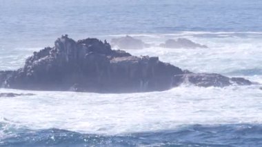 Kayalık okyanus plajı. Büyük dalgalar kayalıklara çarpıyor, mavi su sıçrıyor, deniz köpüğü. Big Sur yakınlarında doğanın gücü, 17 millik yol. Dramatik deniz manzarası. Point Lobos, Monterey, California sahili, ABD