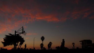 Basketbol oynayan insanlar, basketbol sahasındaki oyuncuların siluetleri, günbatımı okyanus sahili, California sahili, Mission plajı, ABD. Sokak topu sahasında siyah halka, ağ ve arkabahta.