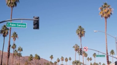 Palmiye ağaçları ve gökyüzü, Palm Springs sokağı, Los Angeles yakınlarındaki şehir, kavşaktaki semafor trafik ışıkları. California çöl vadileri, yaz yolculukları arabayla, Amerika seyahatleri. Dağ. Palm Canyon yol tabelası
