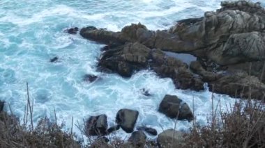 Kayalık okyanus plajı. Büyük dalgalar kayalıklara çarpıyor, mavi su sıçrıyor, deniz köpüğü. Big Sur yakınlarında doğanın gücü, 17 millik yol. Dramatik deniz manzarası. Point Lobos, Monterey, California sahili, ABD