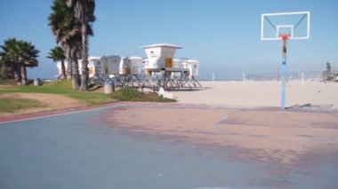Palmiye ağaçları ve basketbol sahası veya Kaliforniya sahillerindeki saha, ABD. Sahilde sokak topu sahası ve cankurtaran durağı, ot istasyonu. Mission Sahili, San Diego. Hoop, sedye ve gökyüzü.