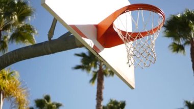 Dışarıda basket oynamak için turuncu halka, ağ ve arka tahta, dışarıda basketbol sahası. Sokak sahasında ya da oyun sahasında eğlence amaçlı spor aletleri. Mavi gökyüzü ve sahil palmiyeleri, Kaliforniya ABD.