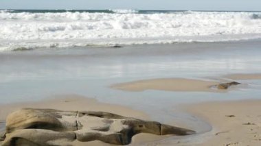 Büyük okyanus dalgaları sahile çarpıyor, La Jolla sahili, California sahili, ABD. Pasifiğin kumlu kıyı şeridinde aşınmış taşlar ya da kayalar. Deniz suyu köpüğü sıçraması, yaz estetiği. Deniz manzarası veya manzarası