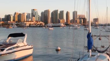Yat marinada ve şehir merkezinde günbatımında ufuk çizgisi, San Diego şehir manzarası, California sahili, ABD. Yükselen gökdelenler, körfezde bir tekne, rıhtım güvertesi. Limanda kentsel mimari ve yelkenli.