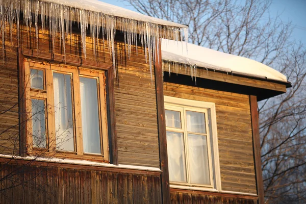 Ghiaccioli sul tetto di una casa di legno con finestre — Foto Stock