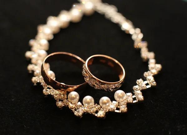 Χρυσά γαμήλια δαχτυλίδια και κολιέ σε μαύρο φόντο — Φωτογραφία Αρχείου