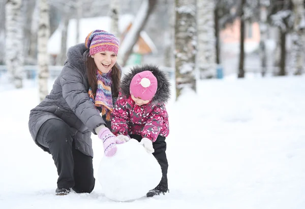 Feliz niña con su madre rodó terrones de nieve, hacer una s — Foto de Stock