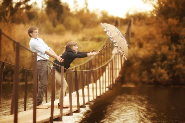 Jóvenes amantes en un puente de cuerda sobre el río bajo el paraguas — Foto de Stock