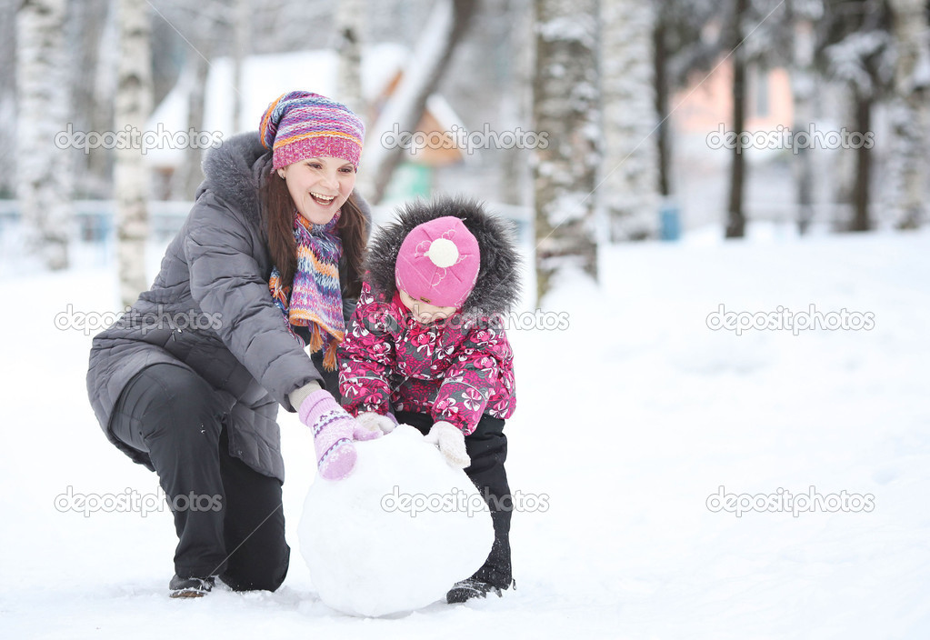 happy little girl with her mother rolled lumps of snow, make a s
