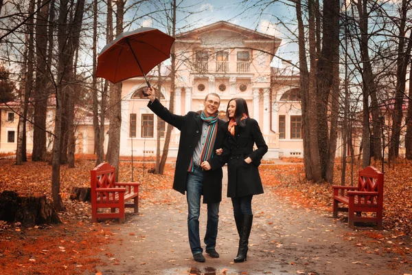 Pareja joven bajo un paraguas en el bosque de otoño — Foto de Stock