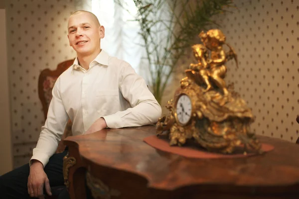 Guy sitting at the table with an antique clock in the old house — Stock Photo, Image