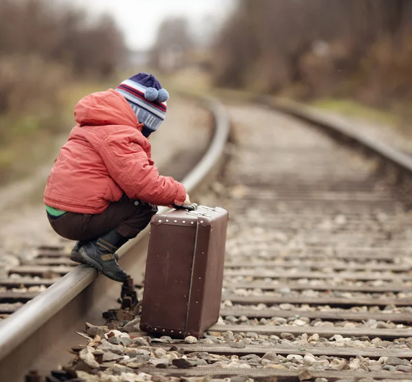 Menino sentado em uma mala perto da viagem ferroviária — Fotografia de Stock