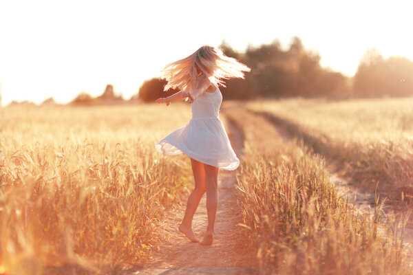Happy girl running on the road in wheat field at sunset