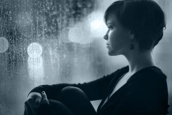 Triste ragazza sul davanzale della finestra guardando fuori dalla finestra — Foto Stock