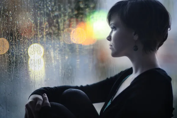 Chica triste en el alféizar de la ventana mirando por la ventana —  Fotos de Stock