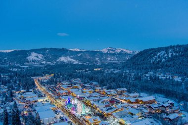 Aydınlatılmış bir Leavenworth, Washington 'un havadan görünüşü ve 2021 yılına yakın çağlayan dağlarını kaplayan kar
