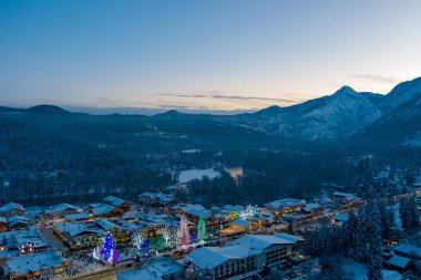 Aydınlatılmış bir Leavenworth, Washington 'un havadan görünüşü ve 2021 yılına yakın çağlayan dağlarını kaplayan kar