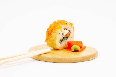 Yuvarlak ahşap bir tabakta kızartılmış suşi rulosu, turşulu pembe zencefil ve beyaz arka planda izole edilmiş yeşil wasabi ile dolu bir hayat. Krem peynirli, balıklı ve soğanlı Tempura dürümü.