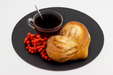 Bir bardak siyah çay ve siyah tepside beyaz arka planda olgun kırmızı Rowan 'la dolu bir kalp şeklinde mayalı çörekle dolu bir hayat. Rus usulü. Üst görünüm