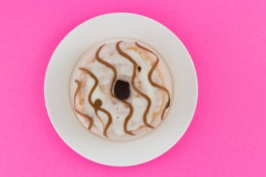 Pembe arka planda izole edilmiş beyaz bir tabakta vanilyalı çörek. Fotokopi alanı ile yaratıcı gıda konsepti. Üst görünüm